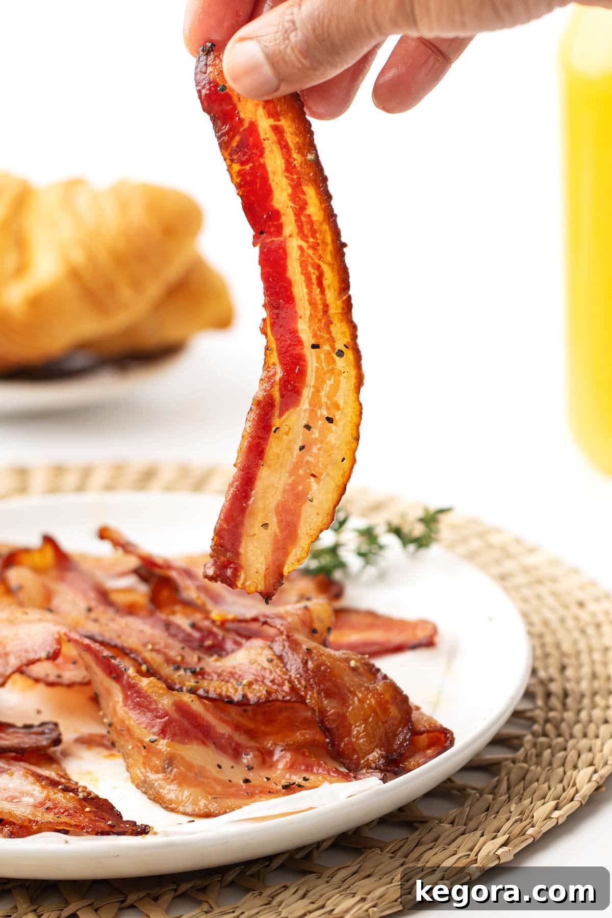 Perfectly Crisp Air Fryer Bacon 2 hand holding a slice of air fryer bacon above plate of bacon