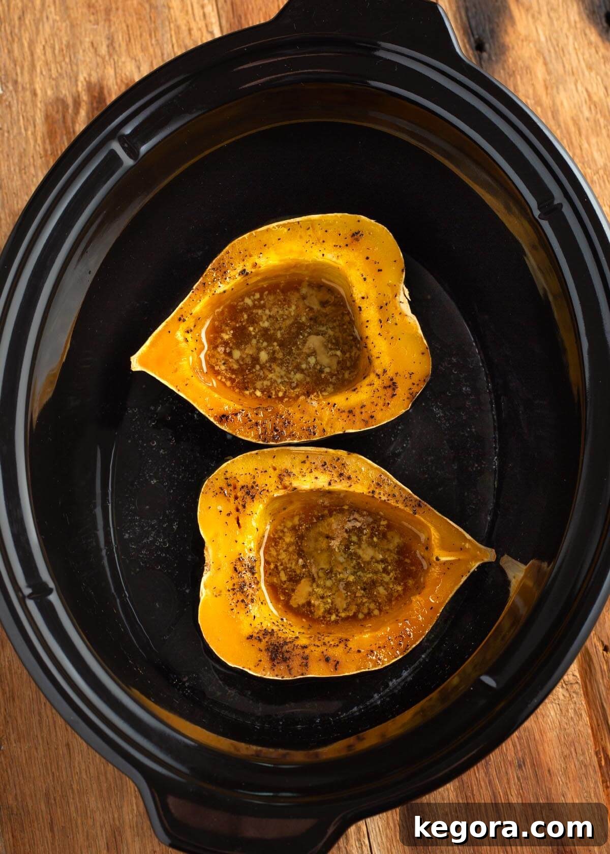 Effortless Slow Cooker Acorn Squash 8 Two acorn squash halves perfectly cooked and nestled in a black slow cooker pot, ready to be removed and served.