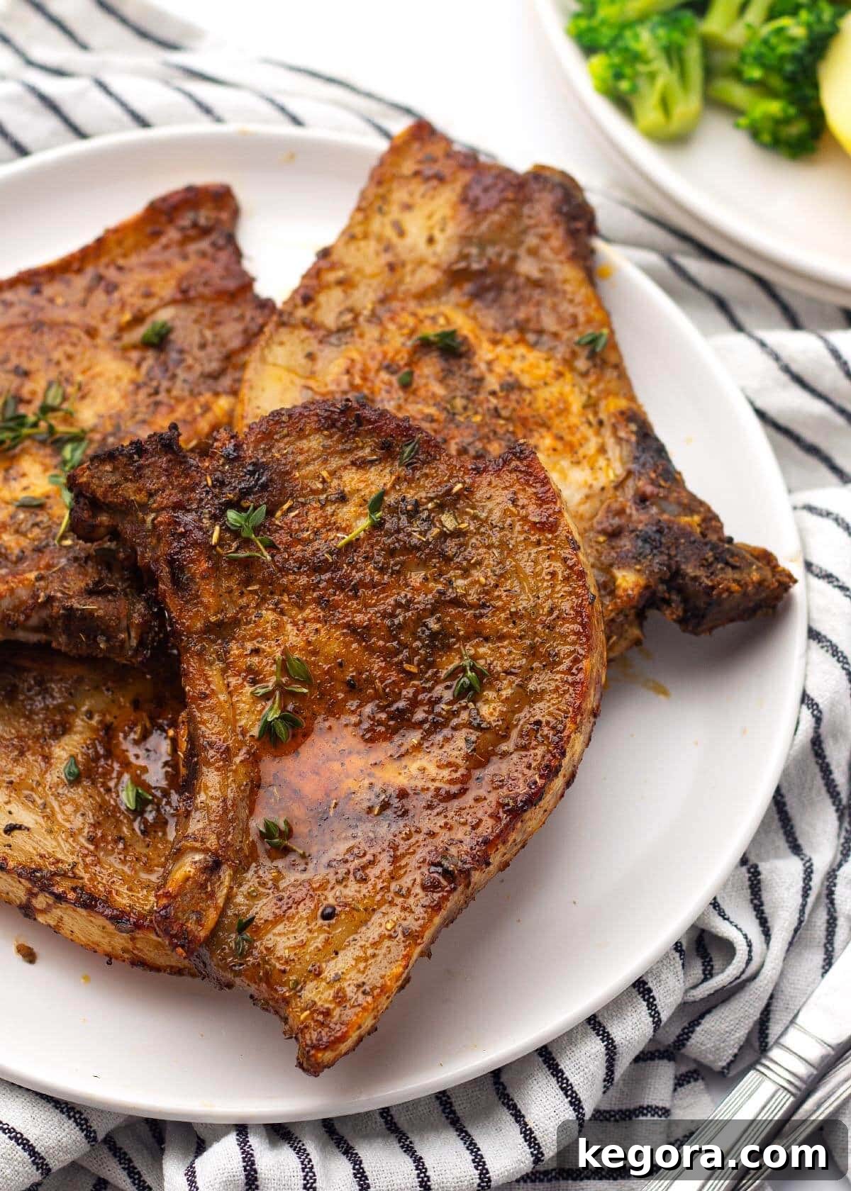Four air fryer pork chops cooked to perfection, showcasing a golden brown crust and promising juiciness, arranged appealingly on a clean white plate.