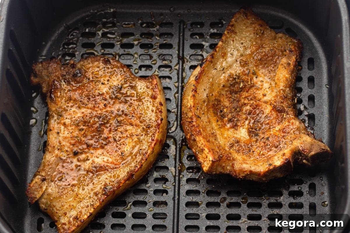 Two cooked pork chops, showing a golden crust and juicy appearance, flipped halfway through cooking in an air fryer basket.
