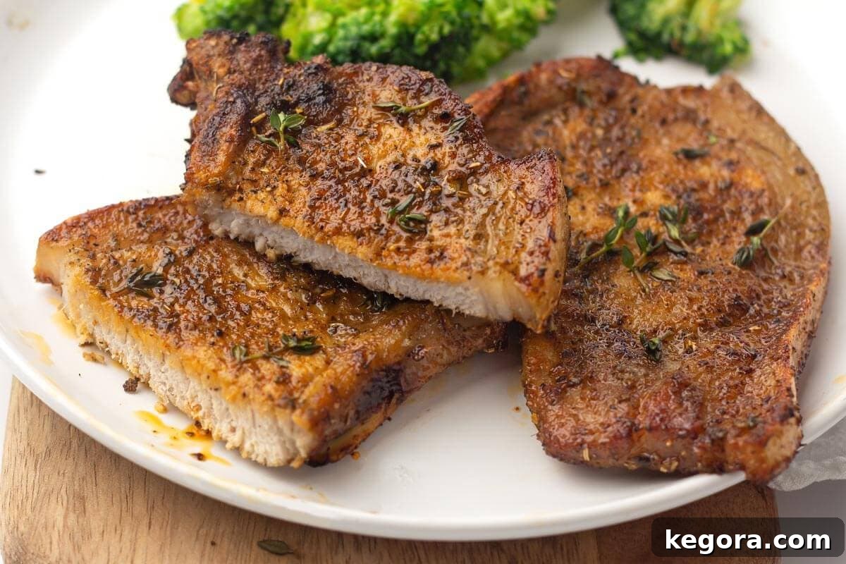 Perfectly cooked air fryer pork chops, golden brown and garnished, served enticingly on a white plate, ready to be enjoyed.