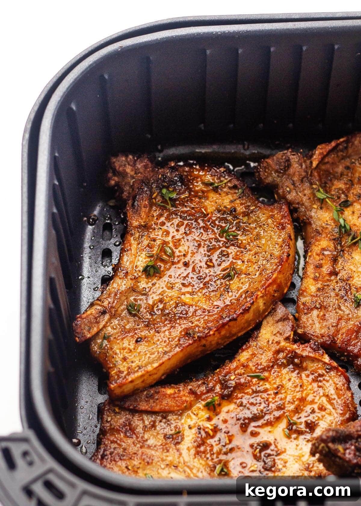 Close-up of seasoned pork chops cooking in an air fryer basket, showing the development of a crispy, golden-brown crust.