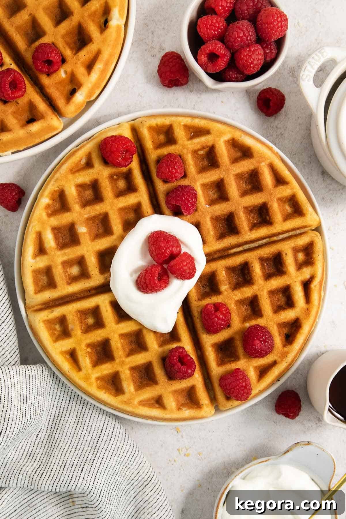 Golden Crisp Gluten-Free Waffles 3 Stack of golden-brown gluten-free waffles on a plate, topped with whipped cream and fresh raspberries.