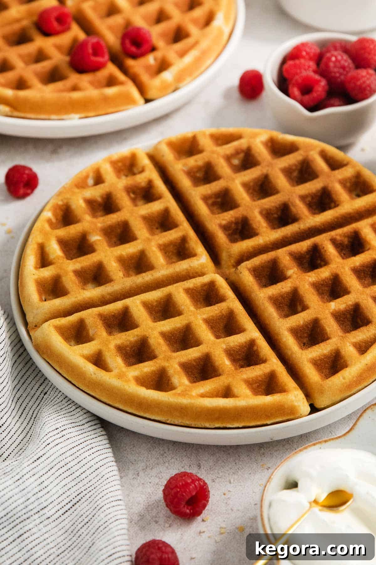 Golden Crisp Gluten-Free Waffles 7 Close-up shot of a gluten-free waffle on a plate, garnished with fresh raspberries, against a kitchen counter background.