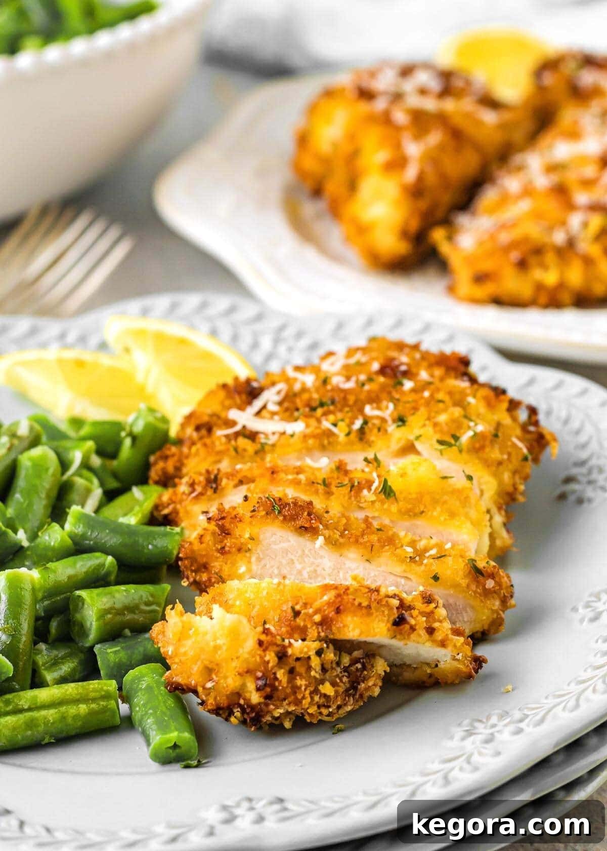 Air Fryer Parmesan Chicken sliced on a plate with green beans and lemon wedge
