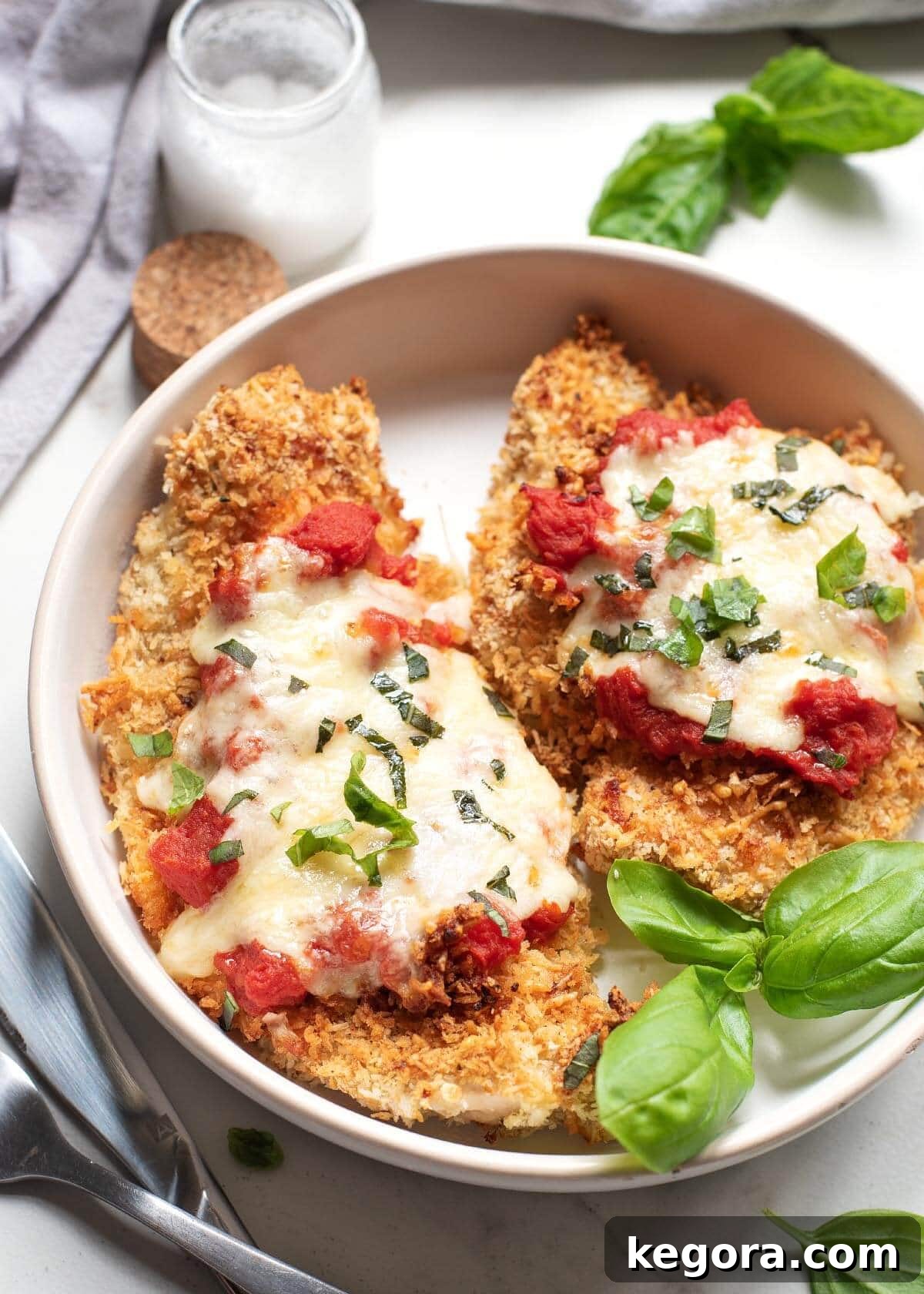 Ultimate Air Fryer Chicken Parmesan 2 Air Fryer Chicken Parmesan on a white plate, garnished with fresh basil.