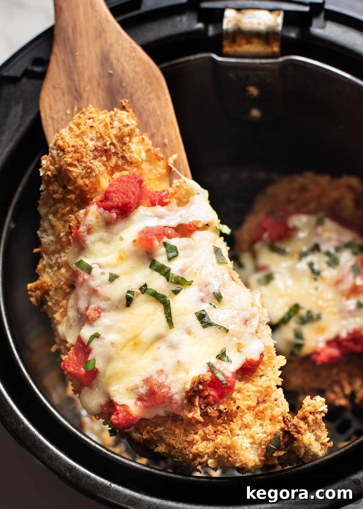 Ultimate Air Fryer Chicken Parmesan 10 Chicken Parmesan in an air fryer basket, being lifted out with a wooden spatula.