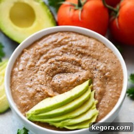 Instant Pot Refried Beans in small white bowl topped with thinly sliced avocado