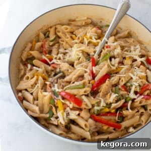 Creamy fajita pasta in a blue skillet, garnished and ready to serve with a spoon.