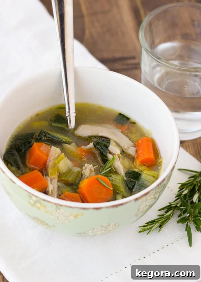 Hearty chicken and vegetable soup in a white bowl with a spoon, accompanied by a glass of water