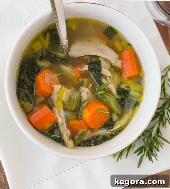Overhead view of a steaming bowl of chicken and vegetable soup with fresh herbs