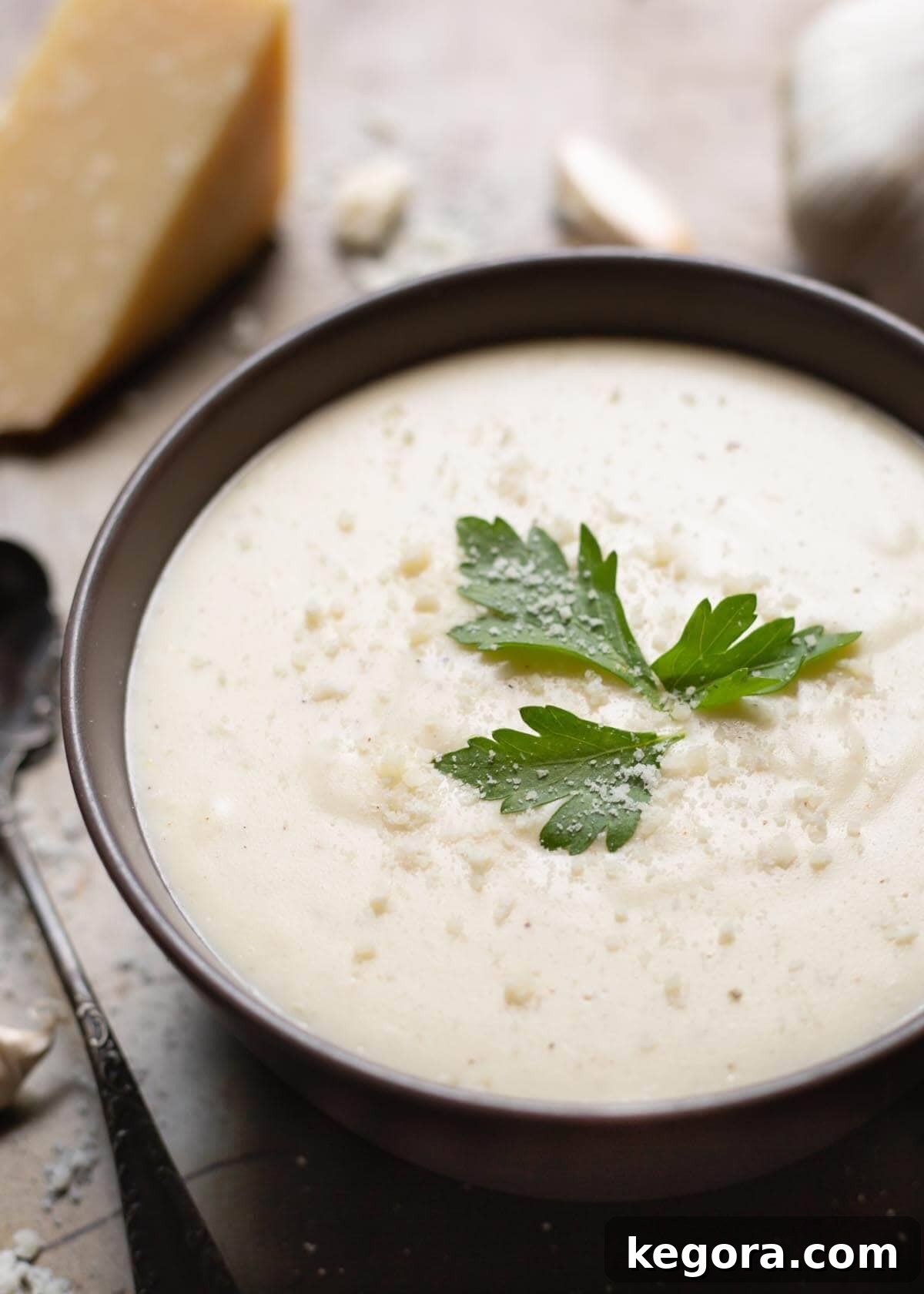 Velvety Garlic Parmesan Sauce 2 Garlic Parmesan Cream Sauce in a black bowl on a wooden board garnished with parsley