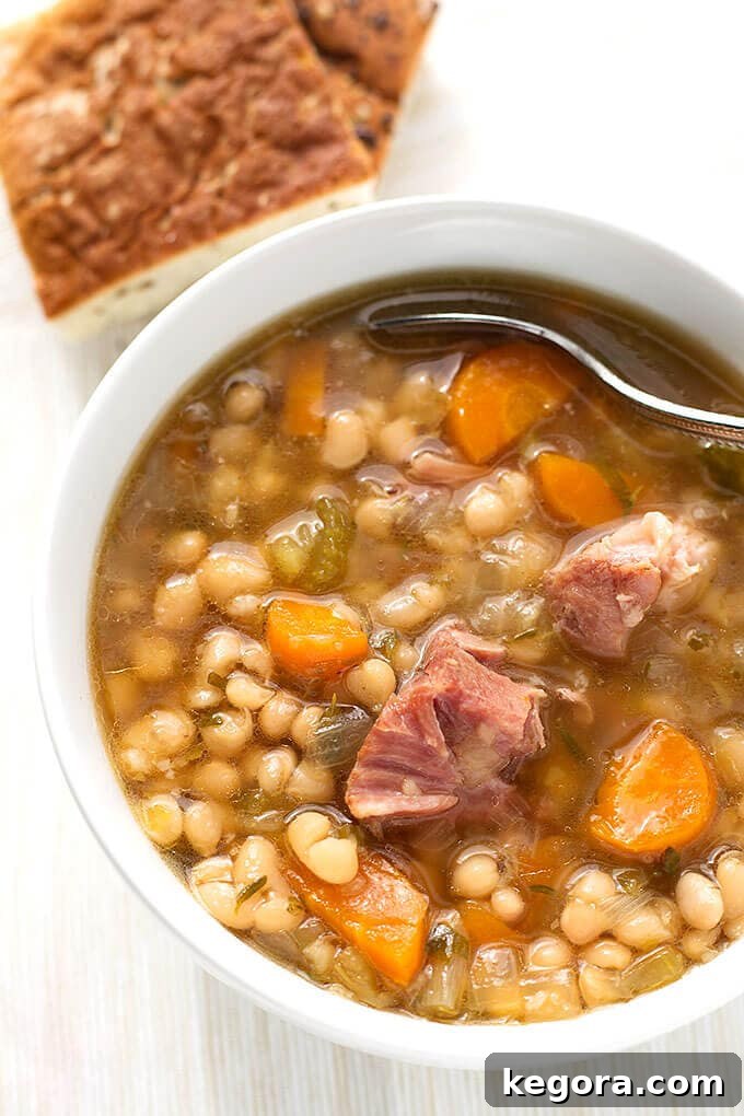 Instant Pot Ham Hock and Bean Soup in white bowl with spoon on white wood background