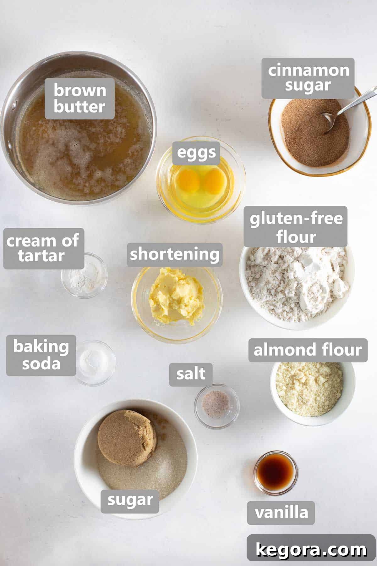 Overhead shot of all the dry and wet ingredients laid out for gluten-free snickerdoodles on a white background, including flour, sugar, butter, and eggs.