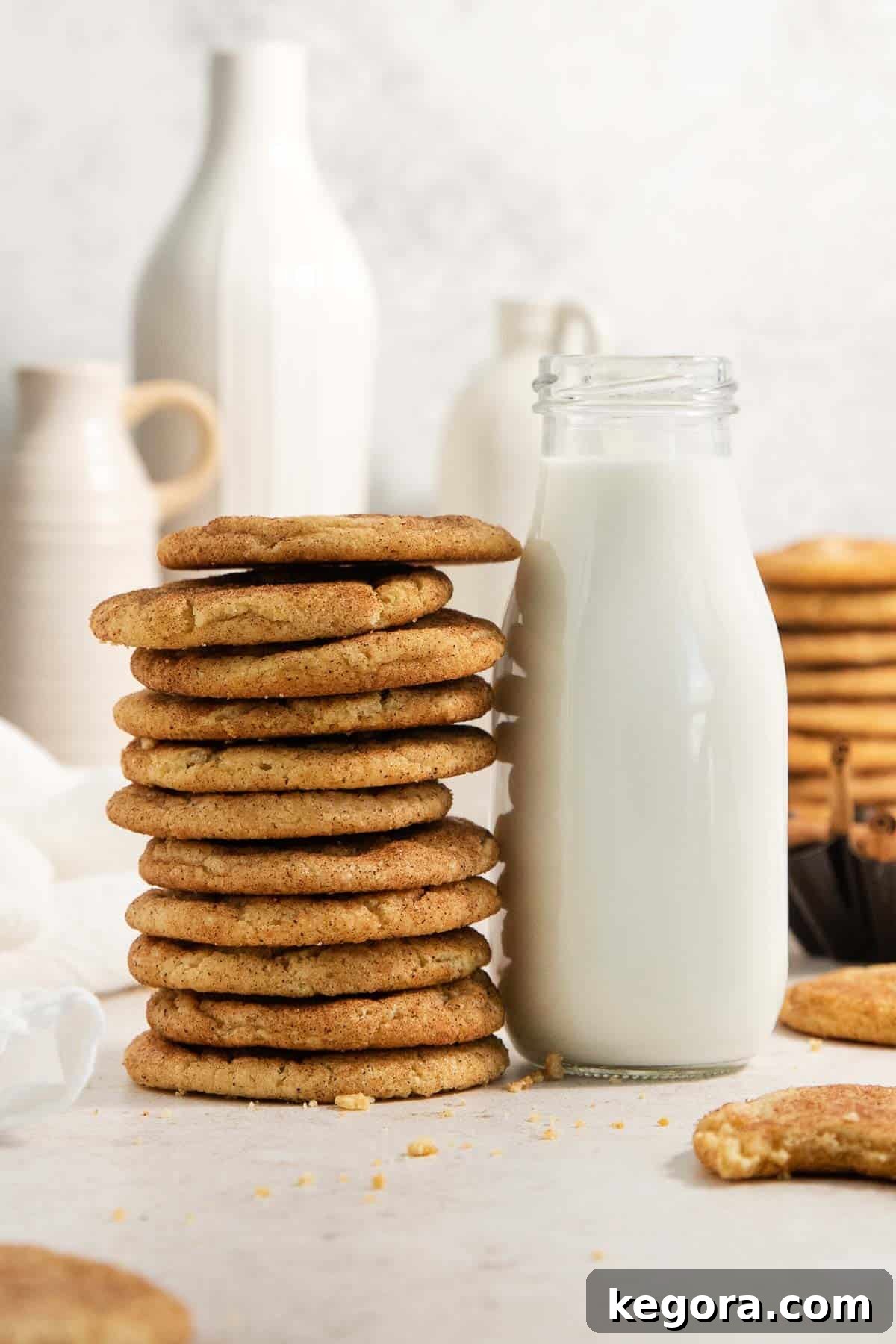 A tower of perfectly baked gluten-free snickerdoodles stacked next to a glass jug of milk, ready to be enjoyed.