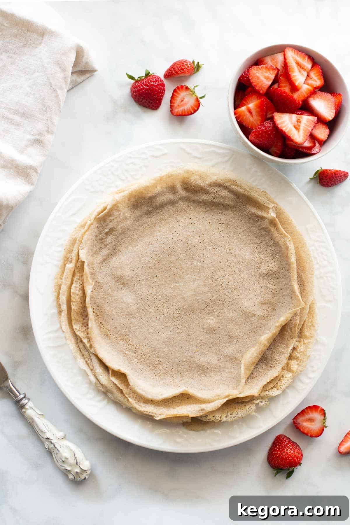 Delicious Gluten-Free Buckwheat Crepes overhead shot of buckwheat crepes on a white plate with strawberries, perfectly golden brown and inviting