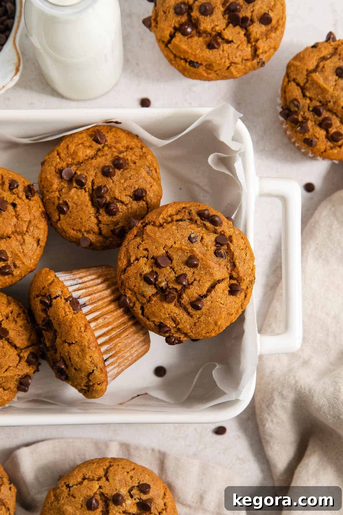 Delicious chocolate chip pumpkin muffins cooling in a baking dish and on the kitchen counter, ready to be enjoyed.