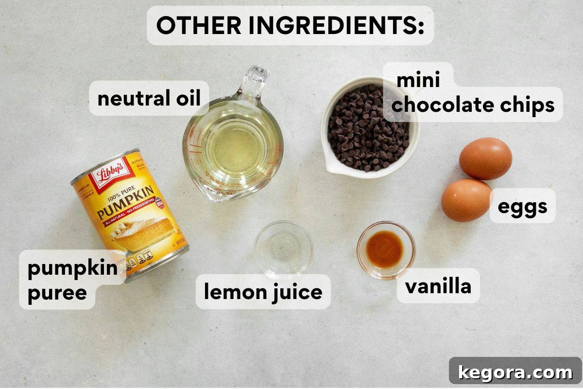 Wet ingredients for pumpkin muffins, including pumpkin puree, eggs, oil, vanilla, and lemon juice, measured and labeled in bowls.