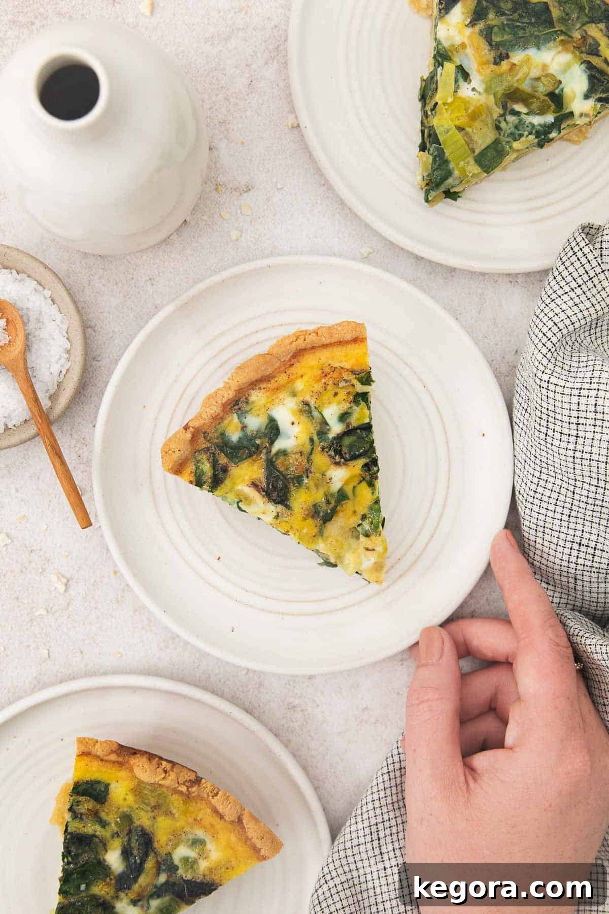 Nutty and Savory Almond Quiche 8 A hand holding a white plate with a generous slice of golden-brown almond flour crust quiche, showcasing its wholesome filling and flaky crust.