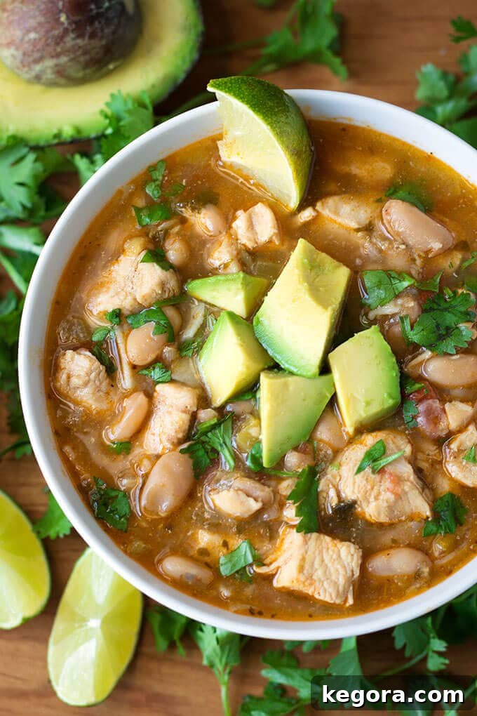 Speedy Creamy Instant Pot White Chicken Chili 2 Instant Pot White Chicken Chili in a white bowl topped with avocado surrounded by cilantro leaves and lime slices