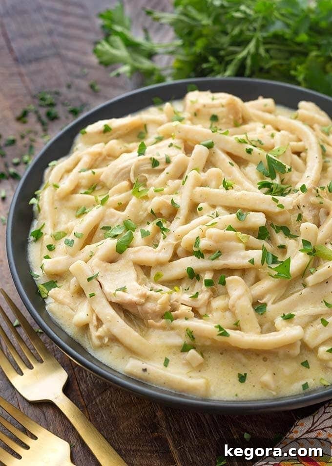 Comforting Instant Pot Chicken Noodles 3 Instant Pot Chicken and Noodles in a shallow black bowl on wooden board next to two golden forks