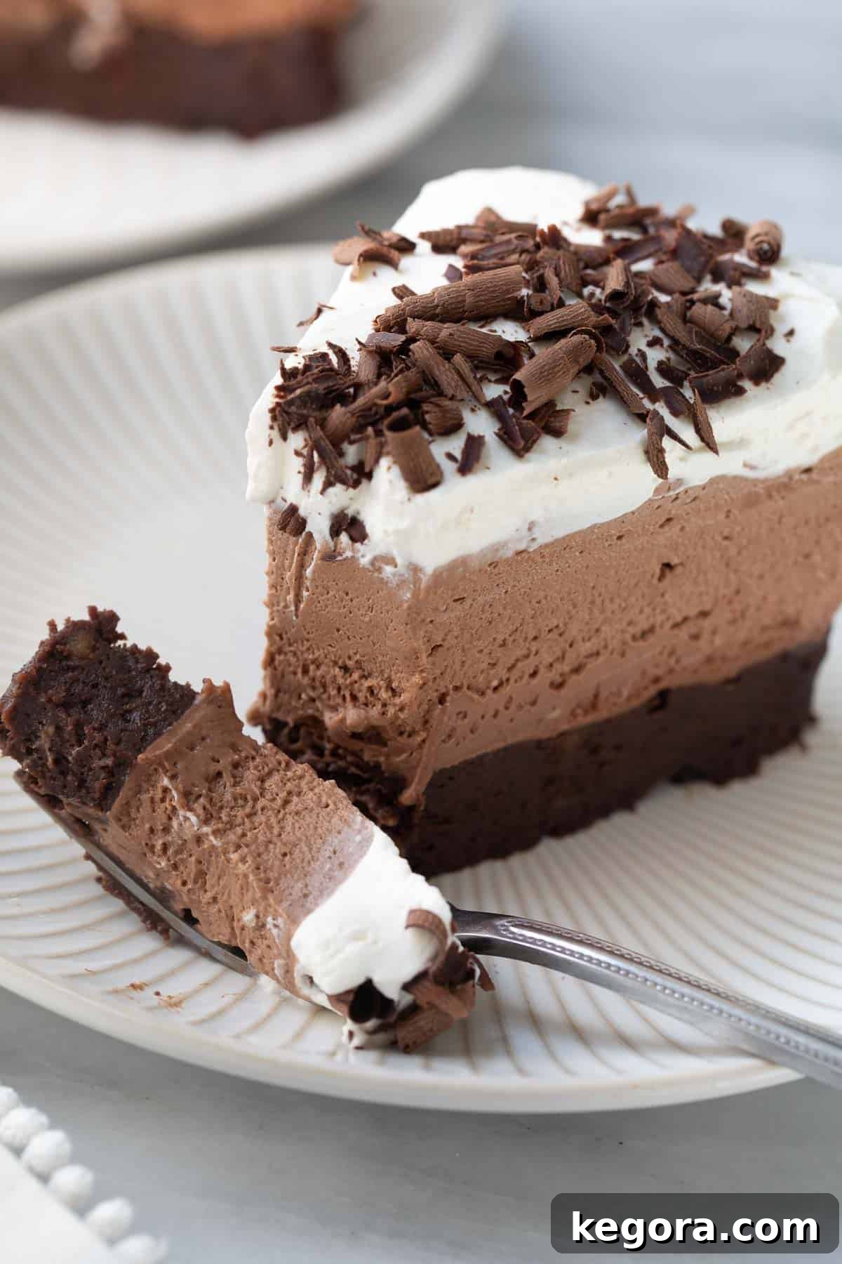 A close-up shot of a magnificent slice of Gluten-Free Chocolate Mousse Cake on a white plate, showcasing its distinct layers and tempting chocolate shavings.