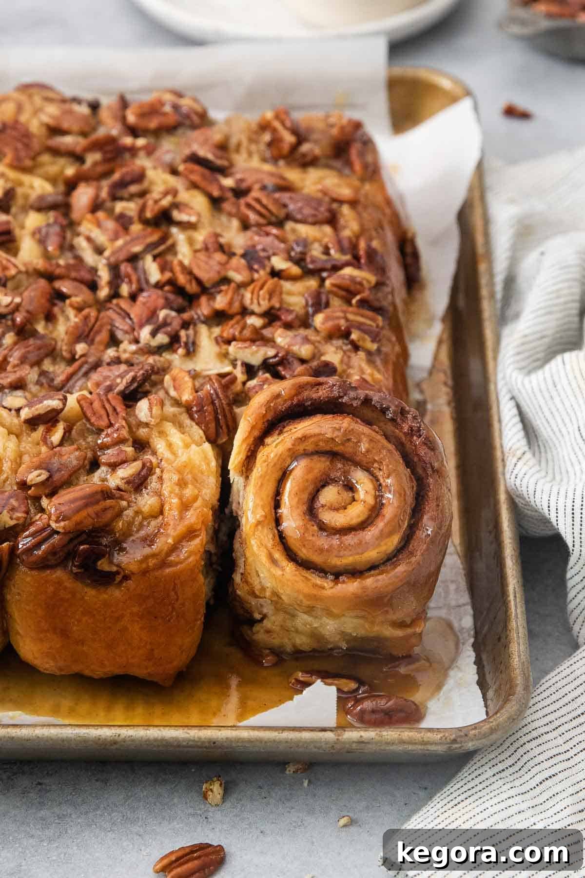 Decadent Gluten-Free Sticky Buns 8 Close-up of baked gluten-free sticky buns on a baking pan, showing the golden tops, gooey caramel, and visible pecan pieces, highlighting their spiral shape.