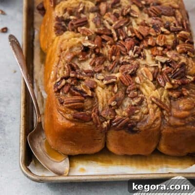 Gluten-free sticky buns on a baking pan with a spoon underneath, ready to be served.