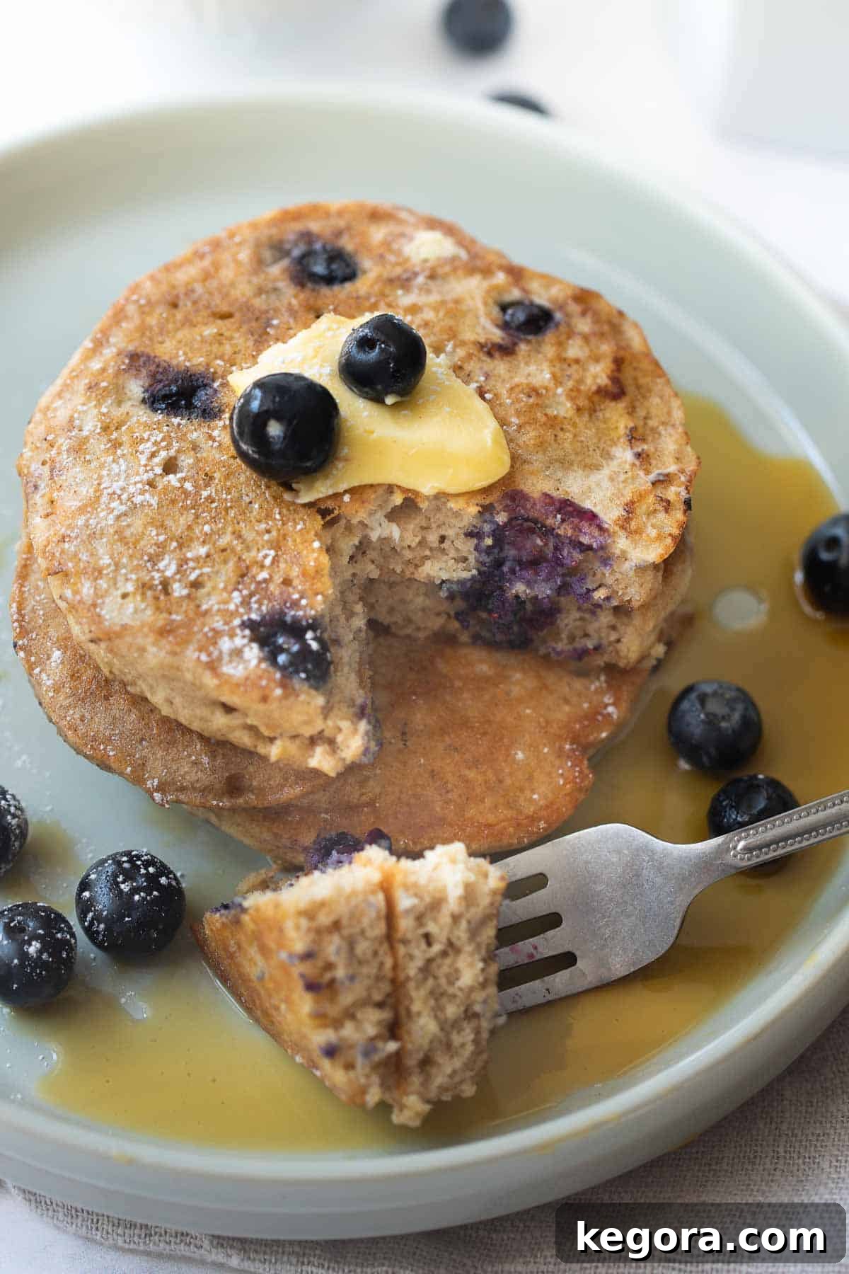 Close-up shot of gluten-free buckwheat blueberry pancakes on a white plate, topped with butter, maple syrup, and fresh blueberries