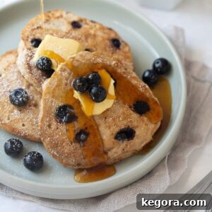 Stack of fluffy gluten-free buckwheat blueberry pancakes topped with butter and maple syrup on a gray plate with fresh blueberries scattered around