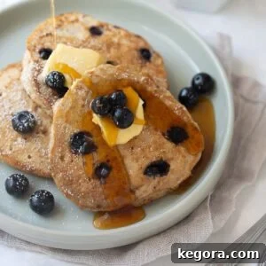 Pancakes on gray plate with blueberries, butter and maple syrup and white background