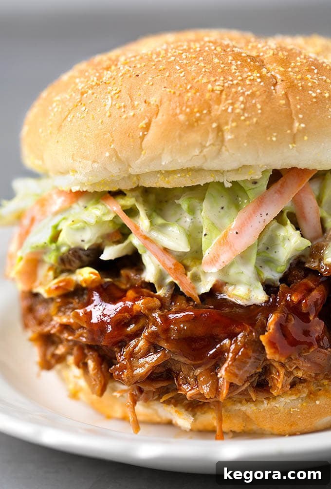 Perfectly Tender Slow Cooker BBQ Pulled Pork 2 Mouth-watering Slow Cooker BBQ Pulled Pork sandwich with creamy coleslaw on a white plate, ready to be enjoyed.