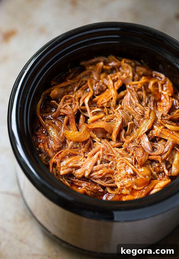Perfectly Tender Slow Cooker BBQ Pulled Pork 3 Juicy BBQ Pulled Pork cooking slowly in a crock pot, tender and ready to be shredded.