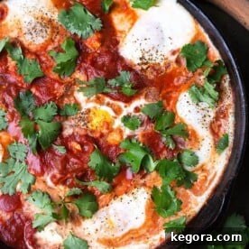 Shakshouka - Eggs in Purgatory in a black bowl next to a wooden spoon