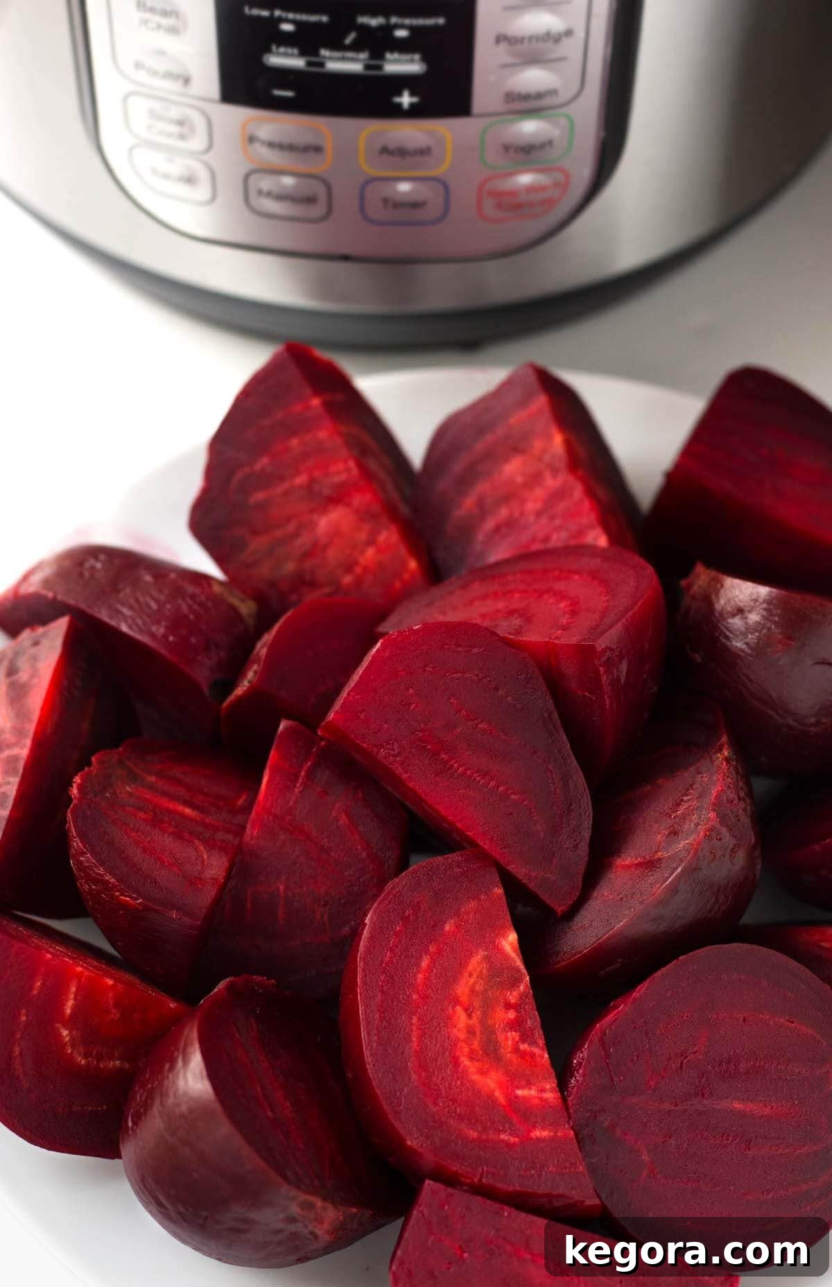 Perfect Instant Pot Beets 2 Cooked quartered instant pot beets on white plate with pressure cooker in the background.