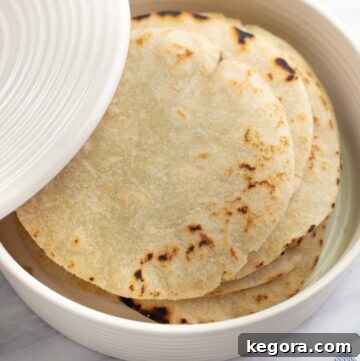 Gluten-free tortillas stacked in a white tortilla warmer on a marble background.
