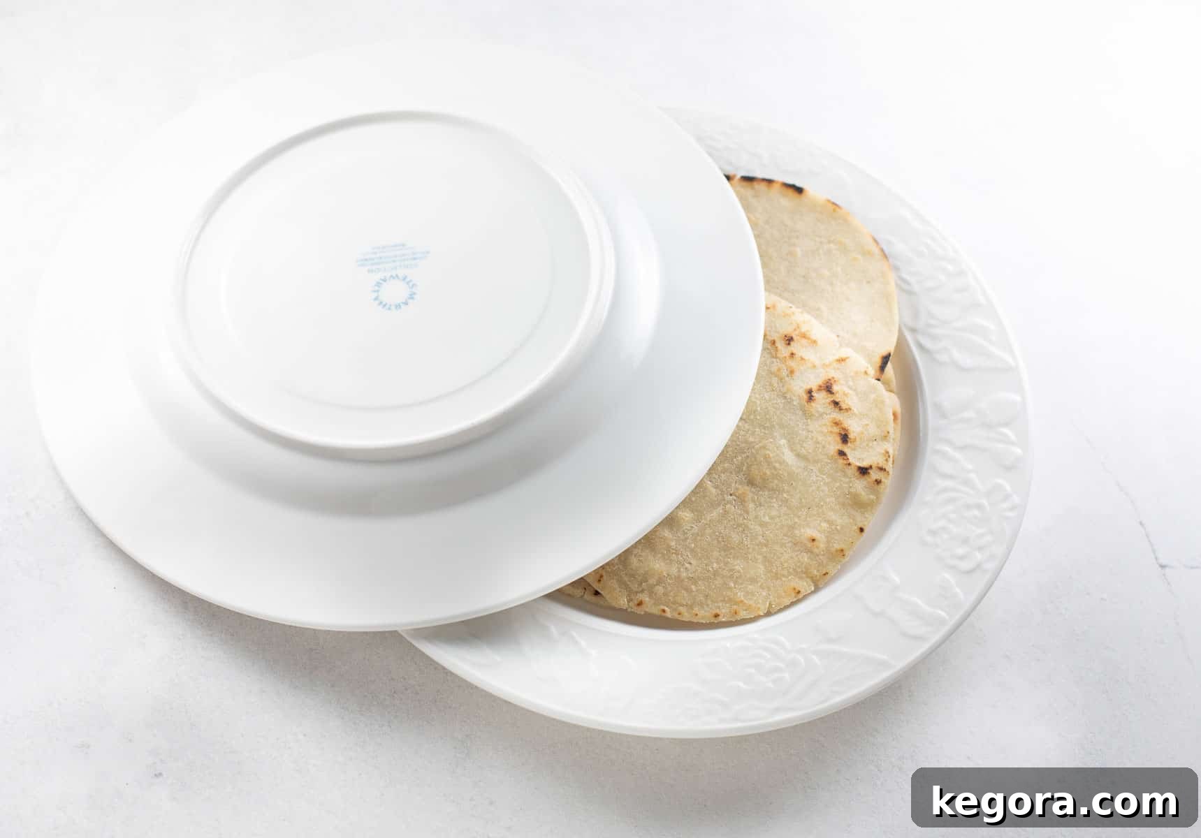 Cooked gluten-free tortillas being stacked between two white plates to keep them warm and soft.