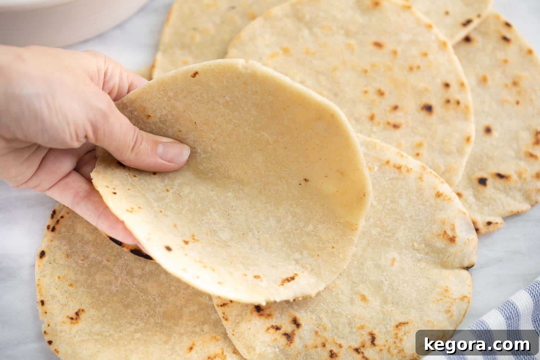 A hand holding a soft, pliable homemade gluten-free flour tortilla, bent in half to show its flexibility.