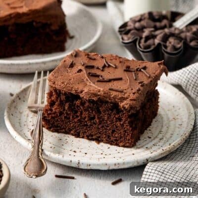A piece of chocolate cake with frosting and sprinkles on a plate with a fork.