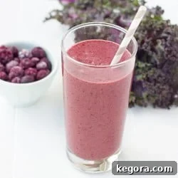 A mixed berry mango kale smoothie in a glass with a straw, accompanied by a bowl of fresh berries.