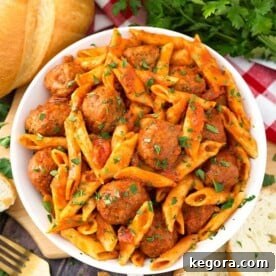 Meatball Pasta Dinner in a white bowl on wooden board next to golden fork and slices of bread