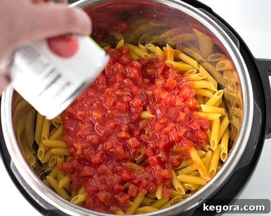 Instant Pot Meatball Pasta Perfection 5 Diced tomatoes carefully added on top of dried pasta in the pressure cooker pot.