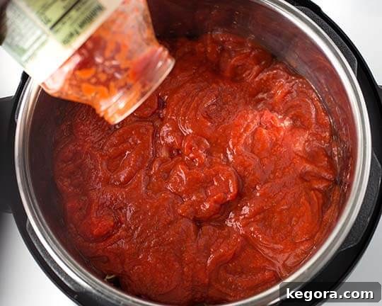 Instant Pot Meatball Pasta Perfection 6 A jar of pasta sauce being poured over the pasta and tomatoes in the Instant Pot, ensuring full coverage.