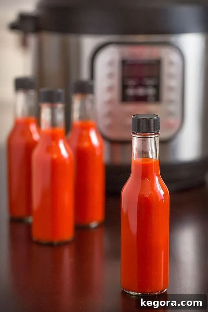 Four bottles of red hot sauce in front of pressure cooker