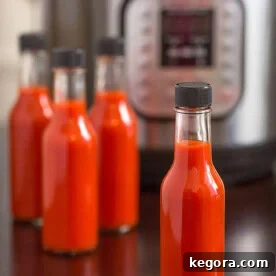 Four bottles of red hot sauce in front of pressure cooker