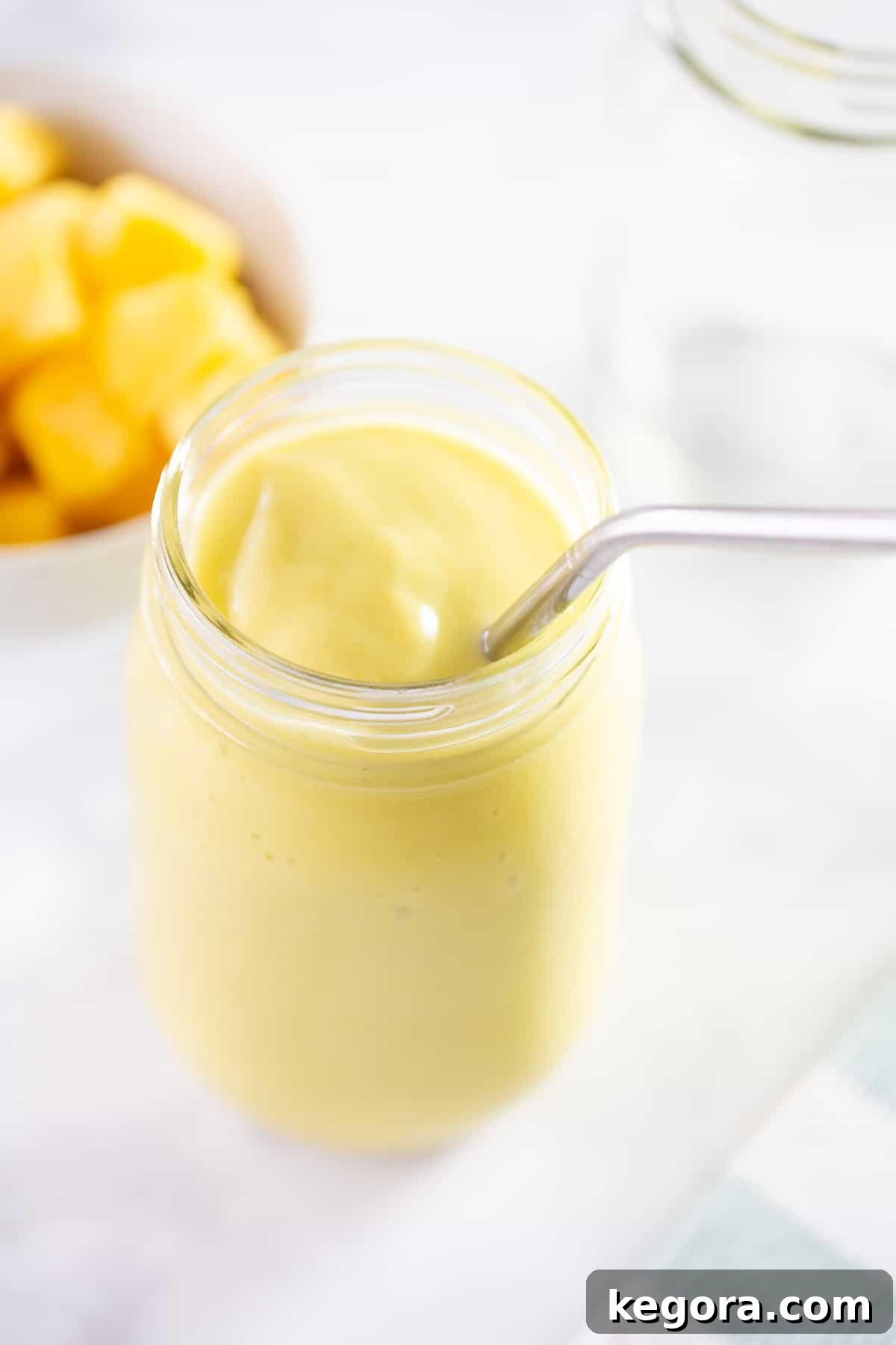 Vibrant mango avocado smoothie in a glass jar with a straw, ready to be enjoyed.