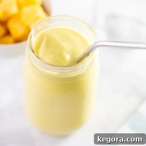 Delicious mango avocado smoothie in a mason jar with a metal straw, garnished.