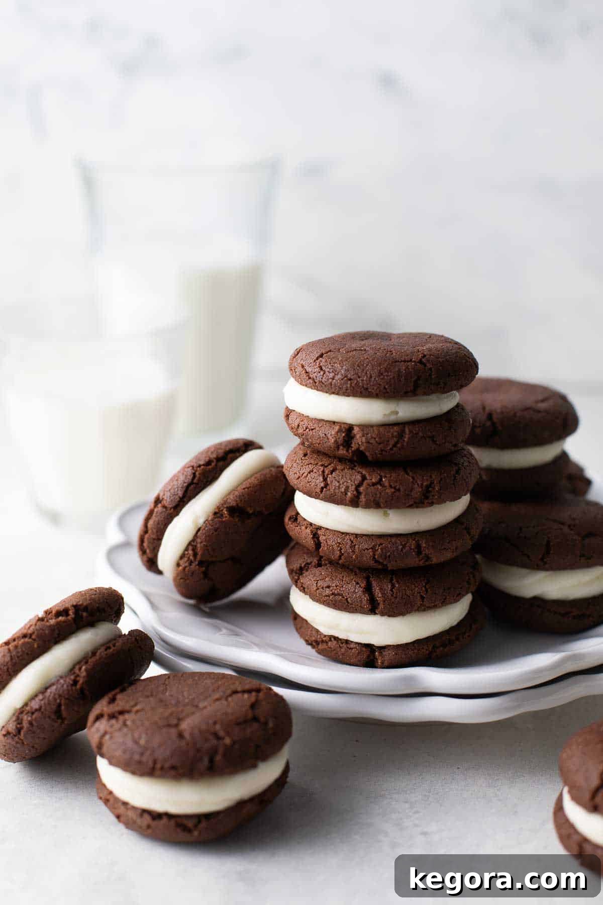 gluten free oreo cookies stacked on white plate with glasses of milk in the background