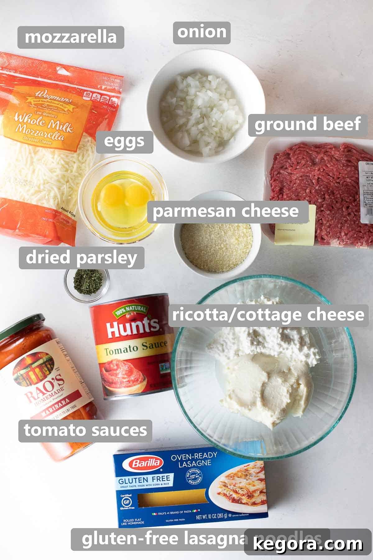 Overhead shot of all labeled ingredients neatly arranged on a white background, including Barilla gluten-free noodles, tomato sauces, ground beef, and various cheeses, for making gluten-free lasagna.