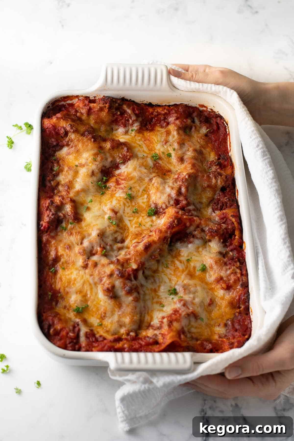A golden-brown gluten-free lasagna just out of the oven, with a white kitchen towel on a marble background.